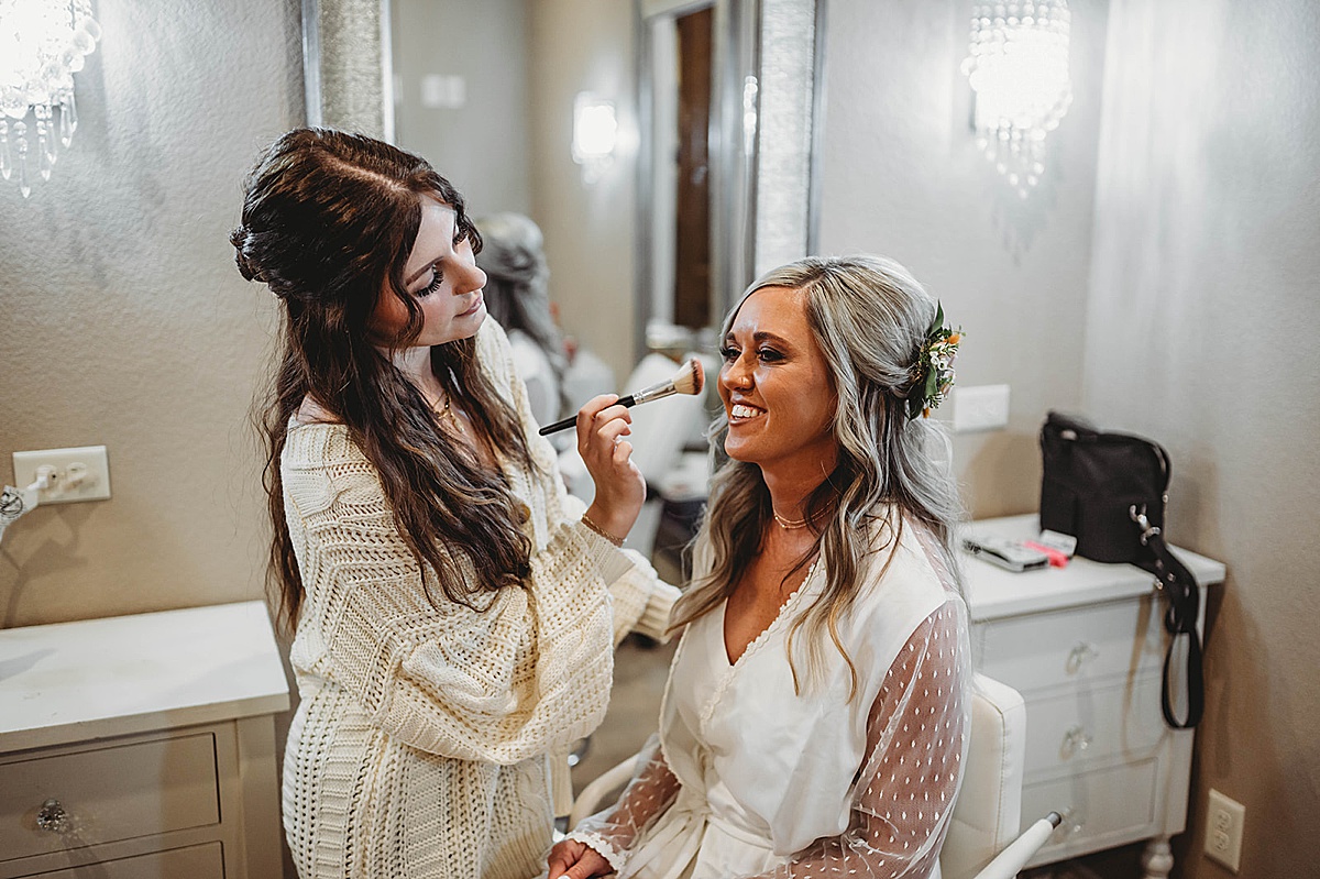 Bride smiles while getting makeup done before boho prairie wedding
