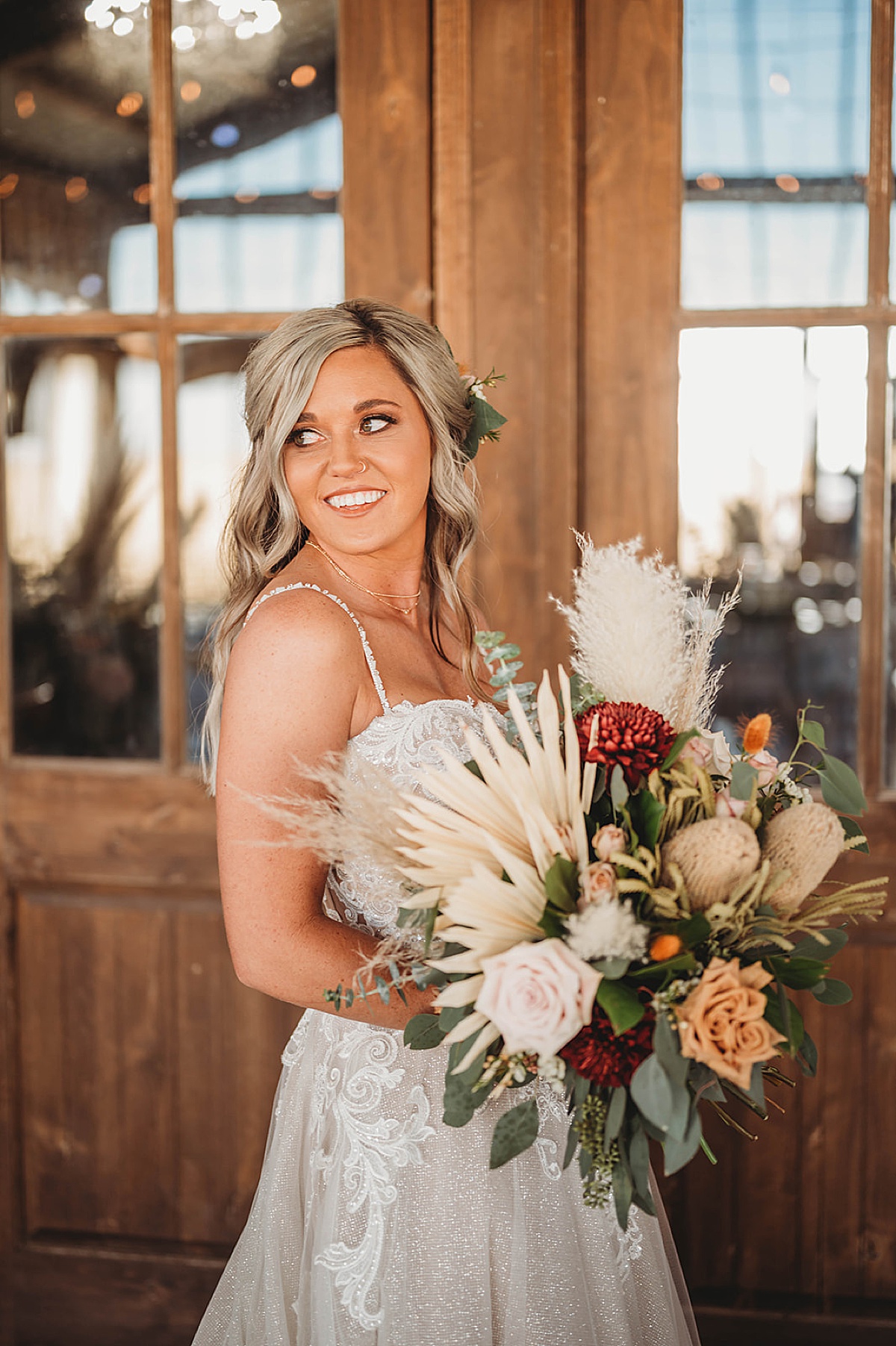 Bride smiles while holding dried flower bouquet outside venue at boho prairie wedding