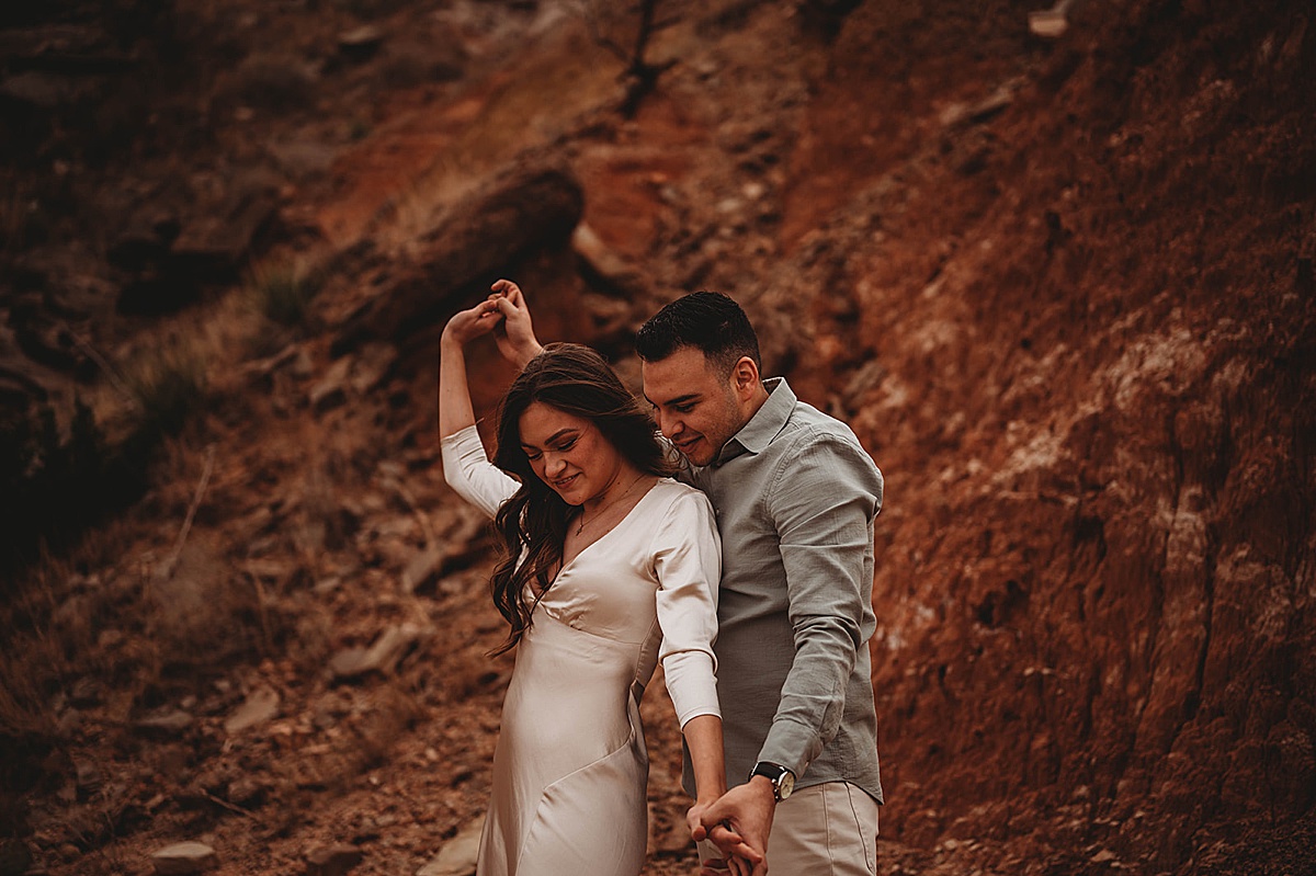 man and woman in white silk dress share romantic dance during canyon adventure engagement shoot