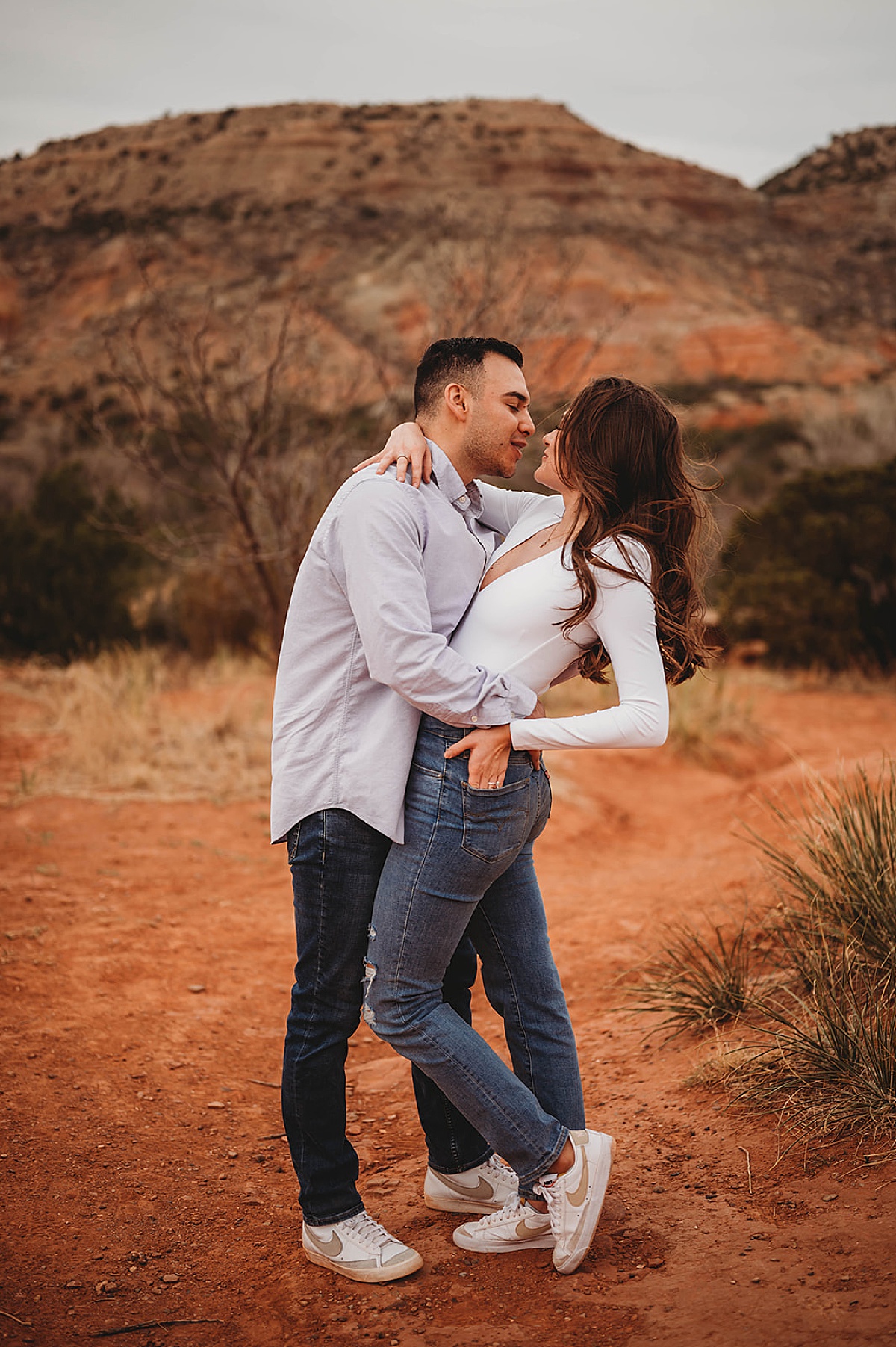 cute couple in jeans and matching sneakers pose during canyon adventure engagement shoot