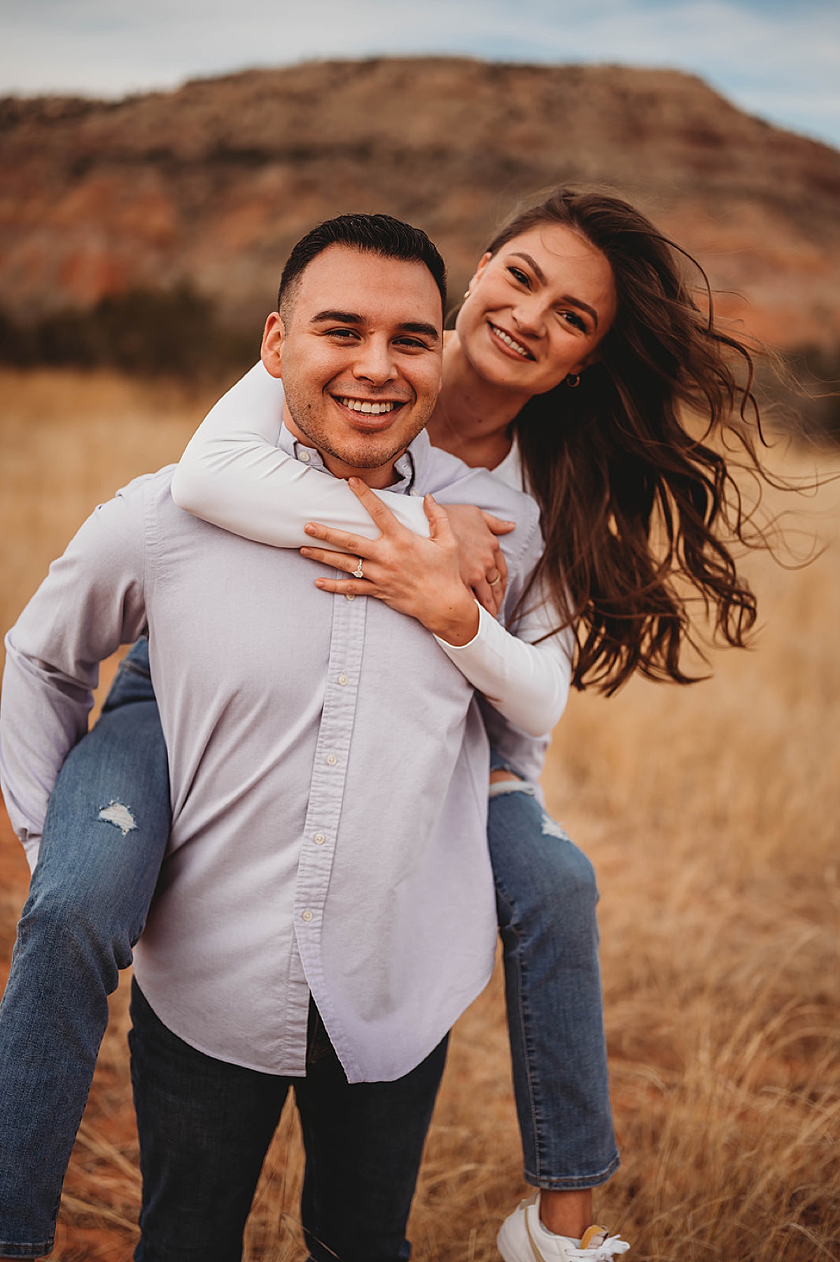 couple in piggy back pose show off diamond ring during canyon adventure engagement shoot