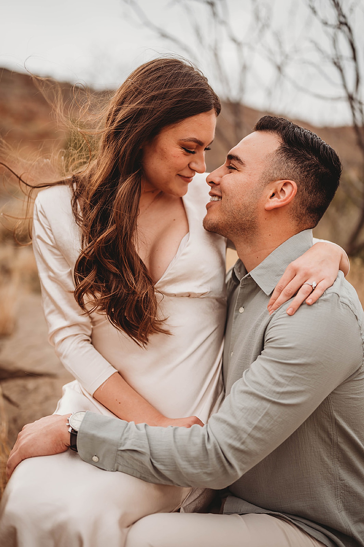 Man and fiancee in white silk dress share a romantic look at canyon shoot by Three Feather Photo Co