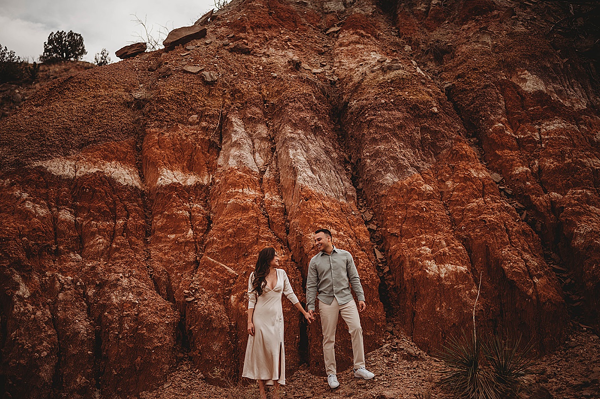 classy couple pose hand in hand in front of red rock cliff shot by Palo Duro Canyon Elopement Photographer