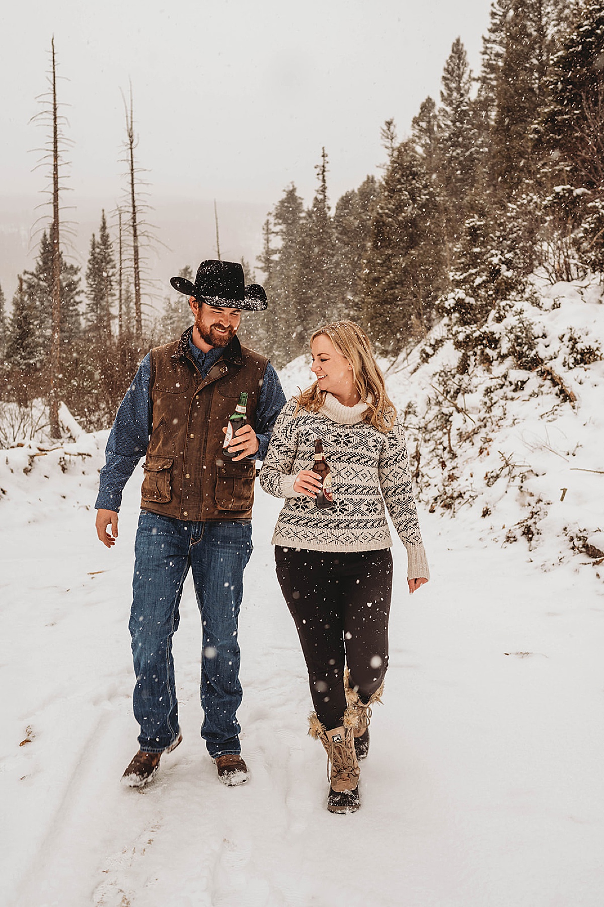 couple strolls mountain road with favorite beers in hand during winter engagement shoot by Palo Duro Canyon Elopement Photographer