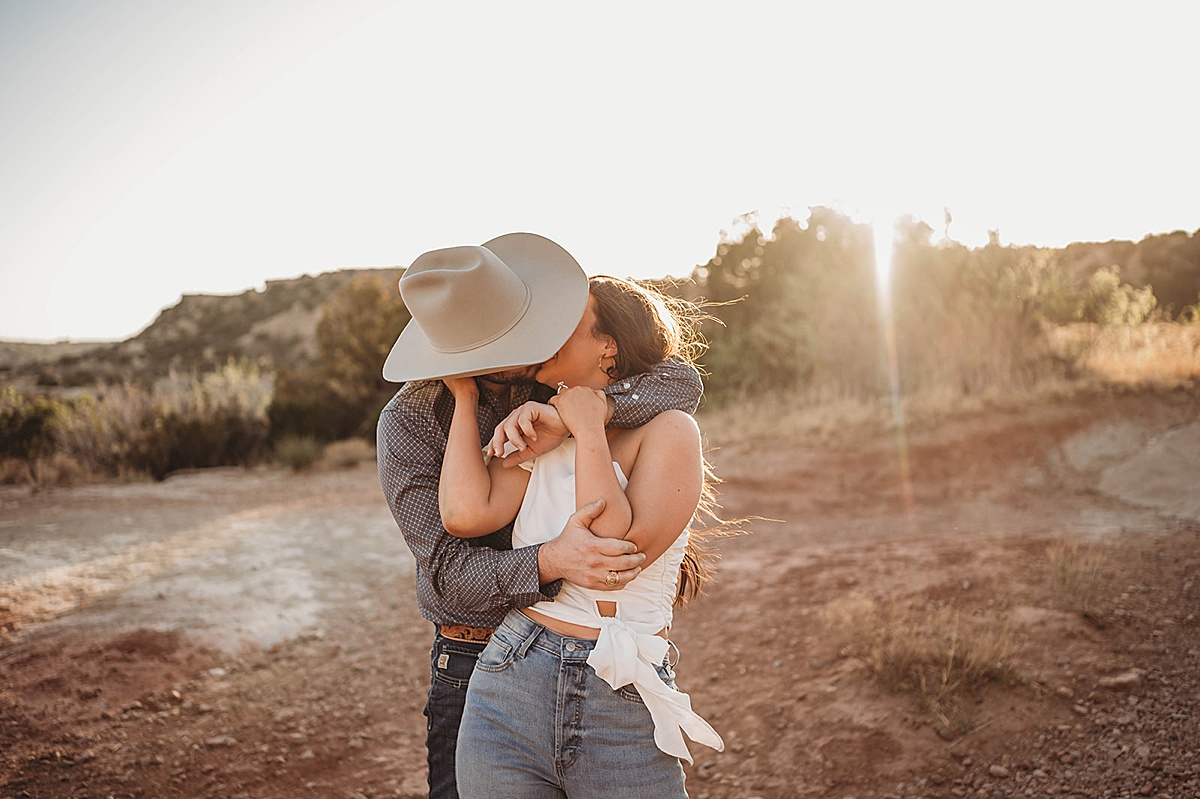 couple in cute white top and cowboy hat kiss during engagement shoot by Three Feather Photo Co