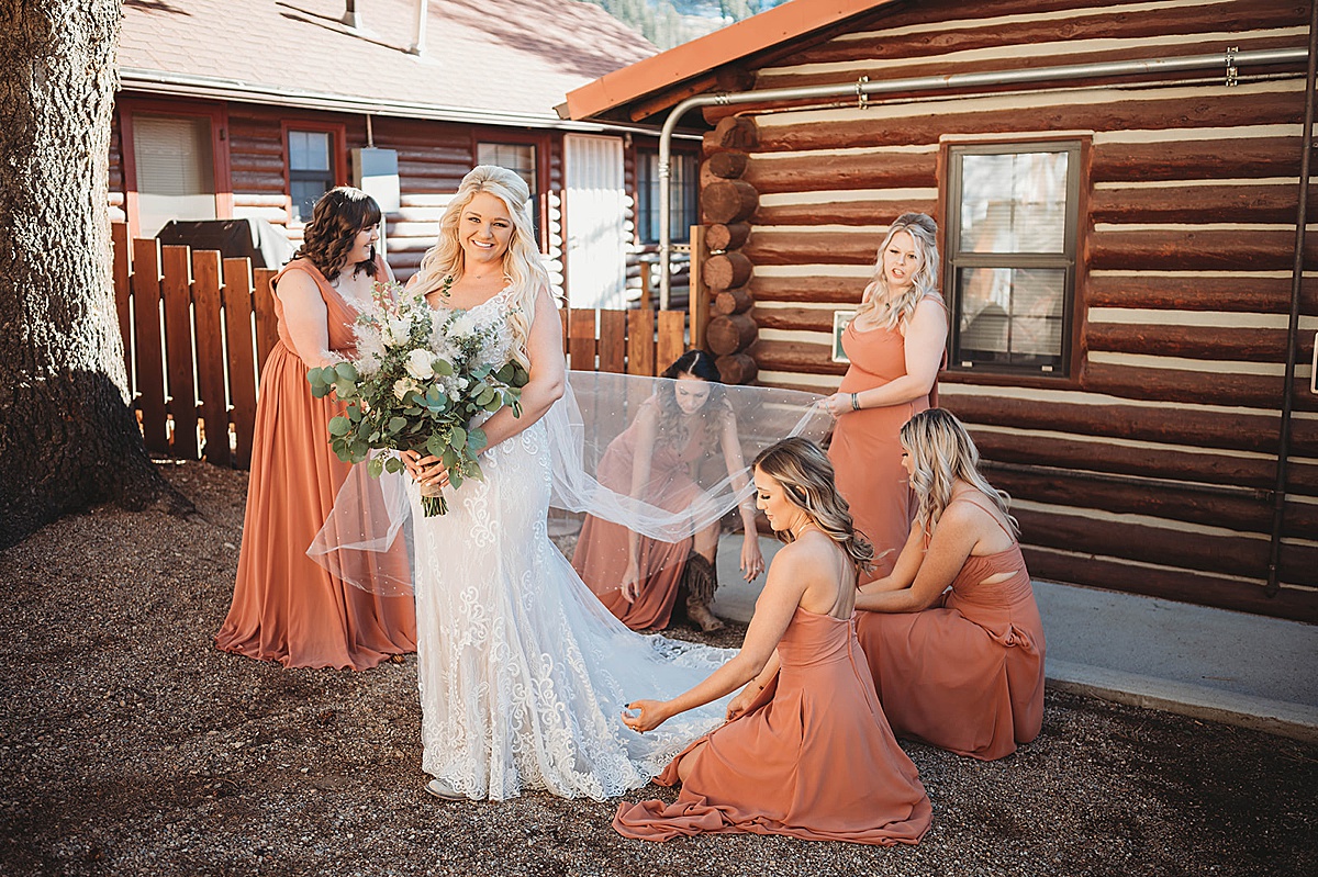 Bridesmaids in warm orange dresses help bride adjust her train and veil before Red River Autumn Wedding