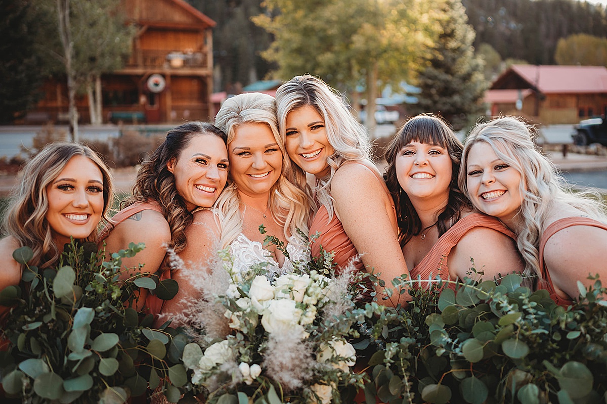 Bridal party poses with bride holding boho bouquets of eucalyptus and white roses before Red River Autumn Wedding