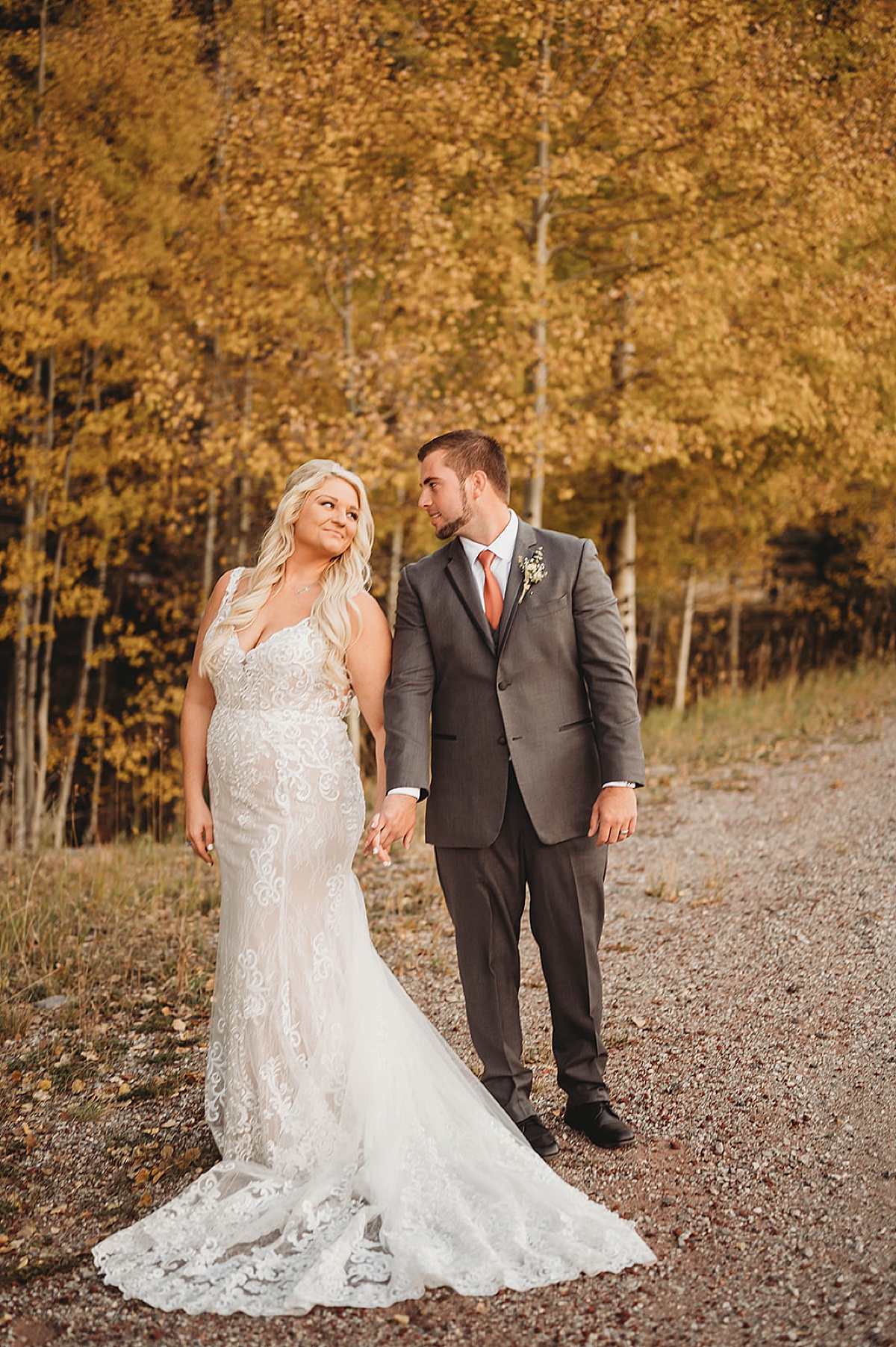 Bride in lace embellished gown and groom in gray suit pose in front of yellow autumn trees shot by palo duro canyon elopement photographer