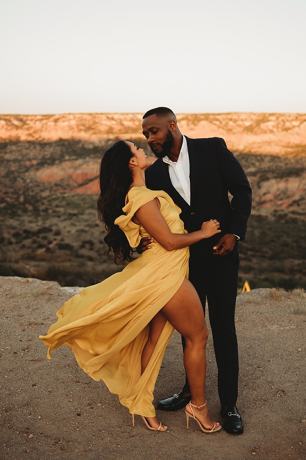 man in black suit and woman in flowy yellow dress pose in glamorous nature engagement shoot