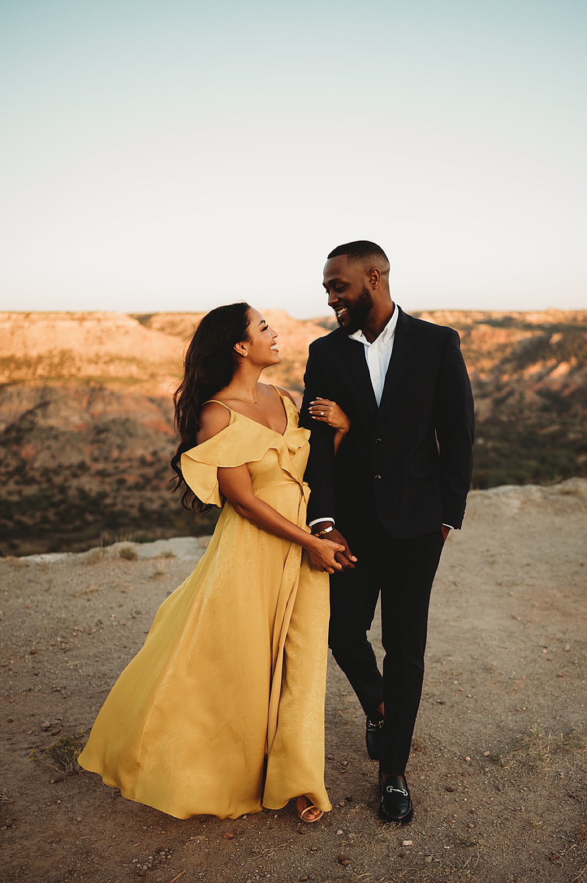 man in evening suit and woman in floor length yellow gown pose in canyon for glamorous nature engagement shoot