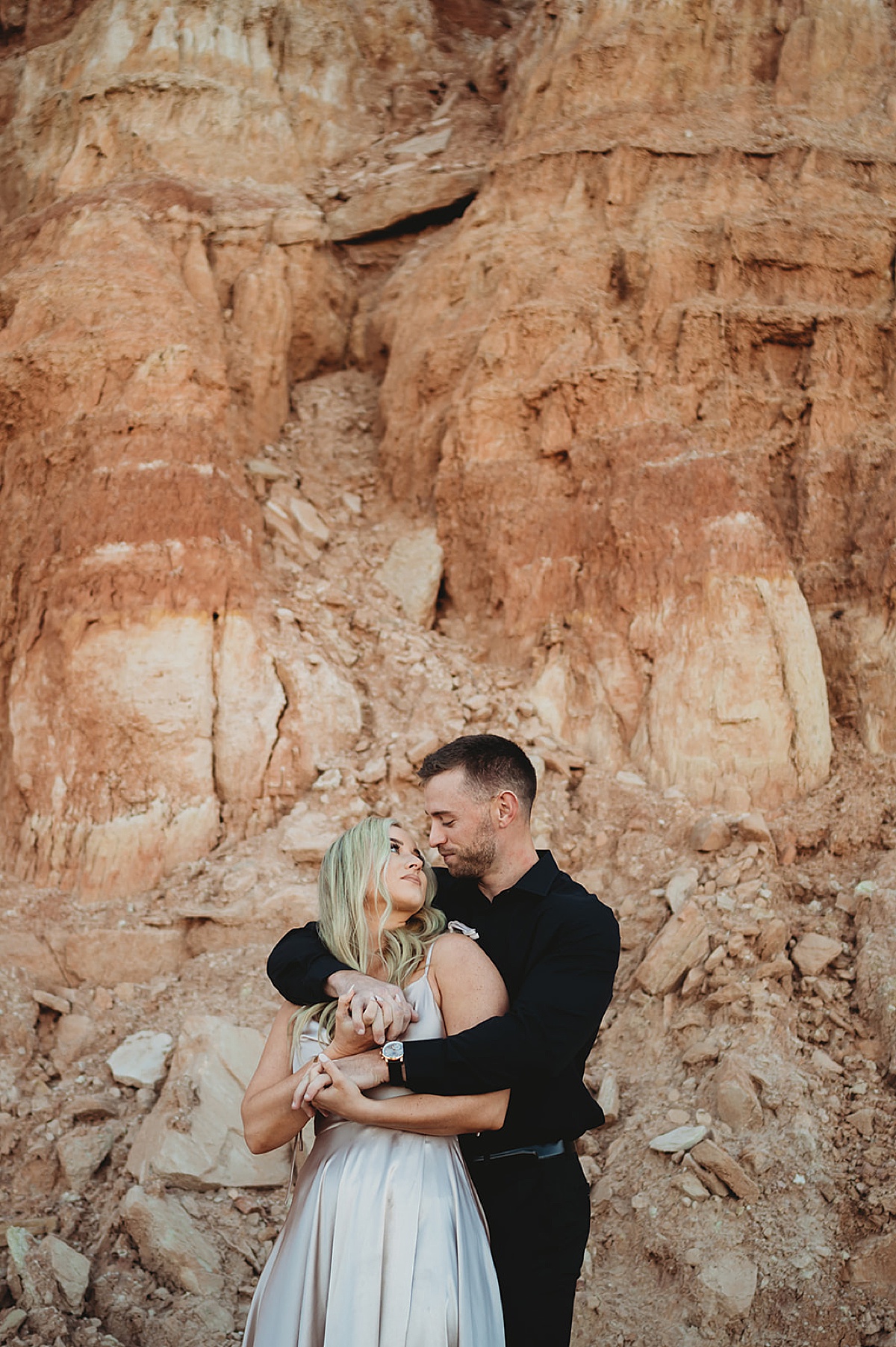couple in evening wear pose in front of red rock canyon during quicksilver and moonlight engagement session