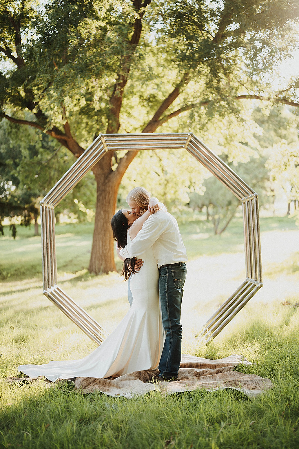 bride and groom kiss during ceremony beneath minimalist geometric arch at sweet summer elopement
