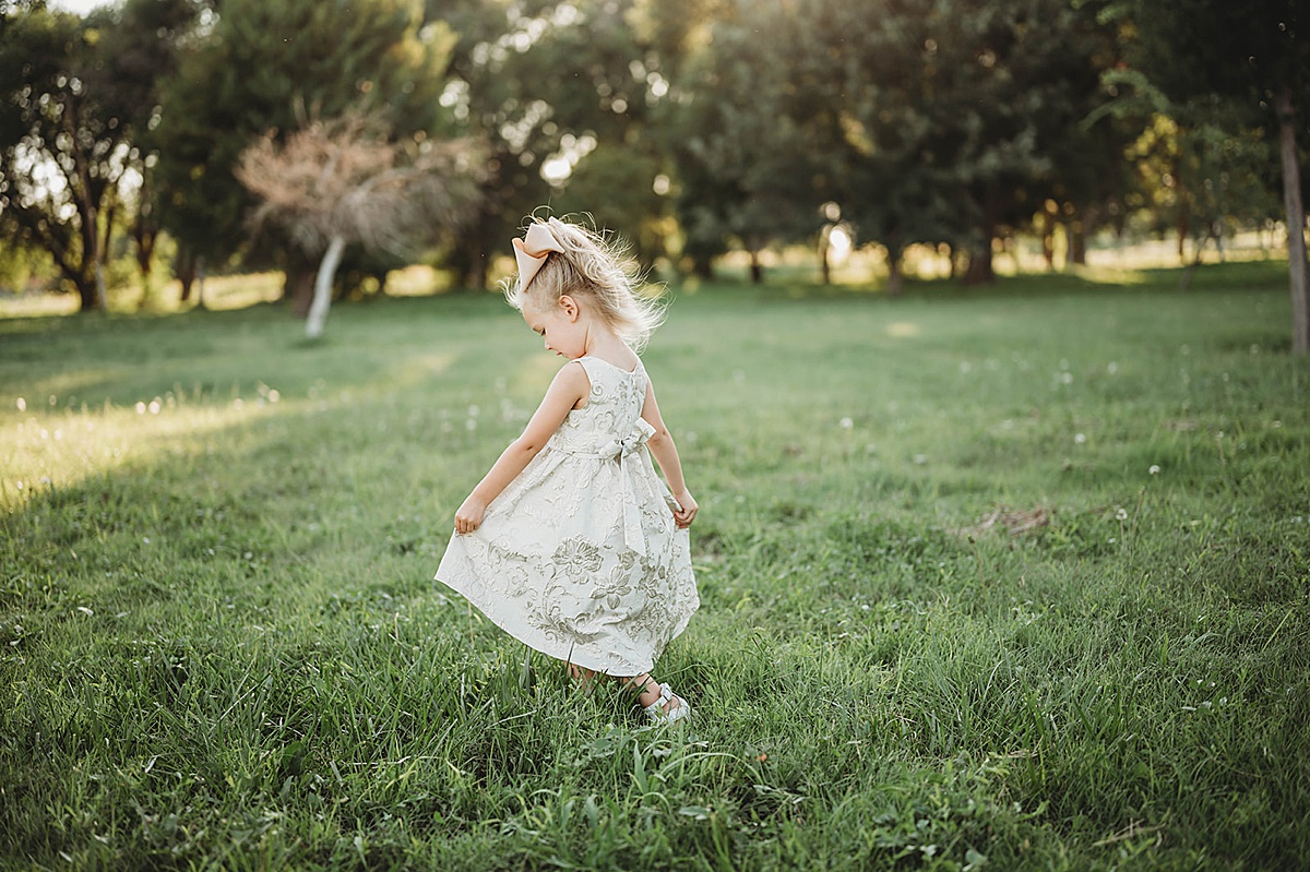 little girl in brocade dress and big hair bow dances through a field during wedding shot by Palo Duro Canyon Elopement Photographer