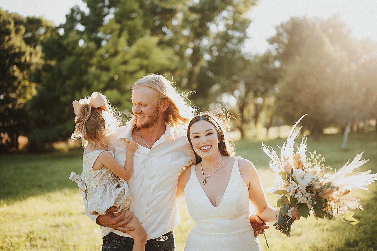 newlywed couple pose in sunny field with their daughter after ceremony shot by Palo Duro Canyon Elopement Photographer
