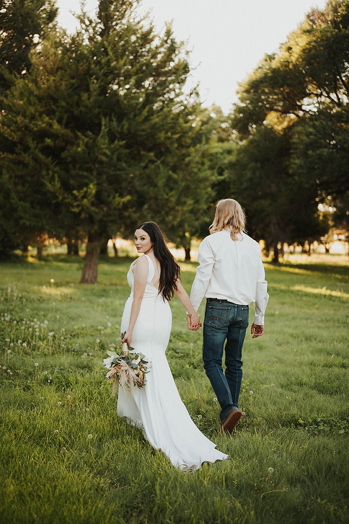 bride looks back over shoulder while walking with groom through lush field shot by Palo Duro Canyon Elopement Photographer