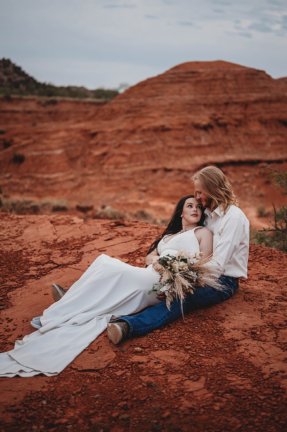 boho minimalist bride with dried flower bouquet leans back on dapper groom in western jeans during shoot with Palo Duro Canyon Elopement Photographer