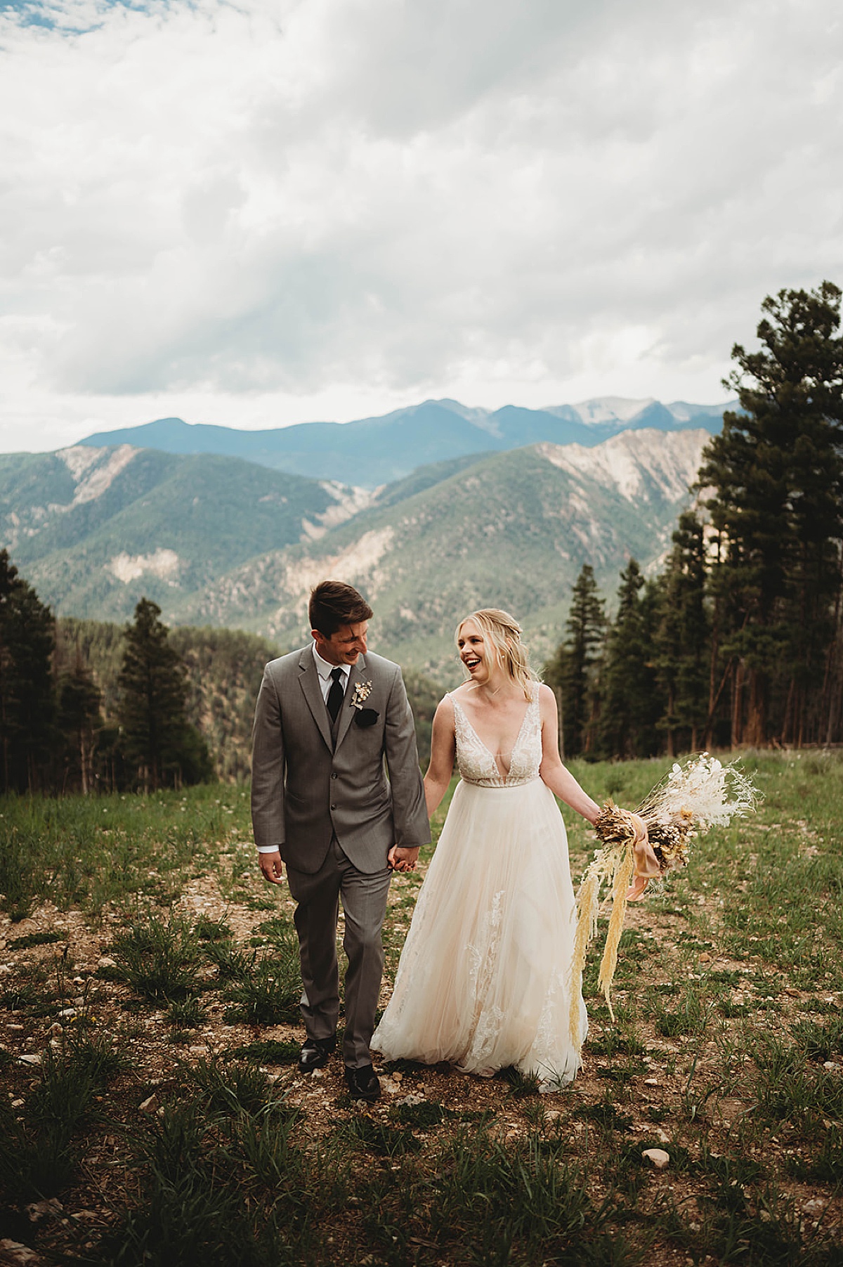 groom in grey suit and bride in lace wedding gown pose during Boho mountain top wedding