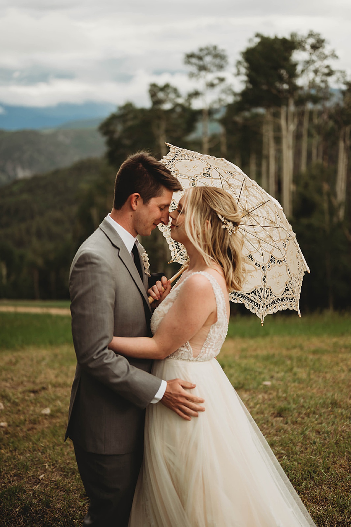 bride and groom pose under lace umbrella during mountain side wedding shot by Three Feather Photo Co