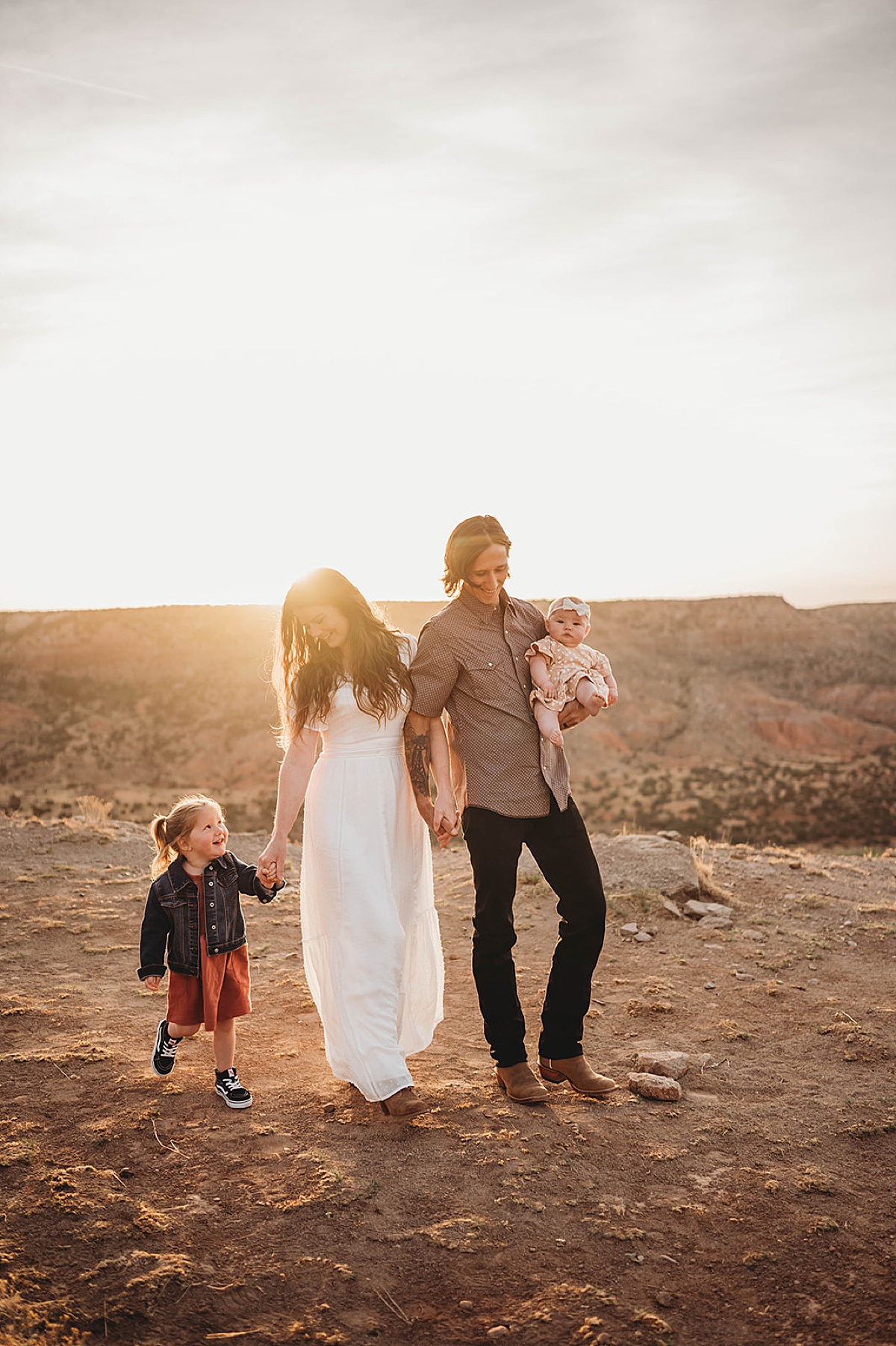 young husband and wife with two daughters pose in canyon during sunrise adventure family portraits
