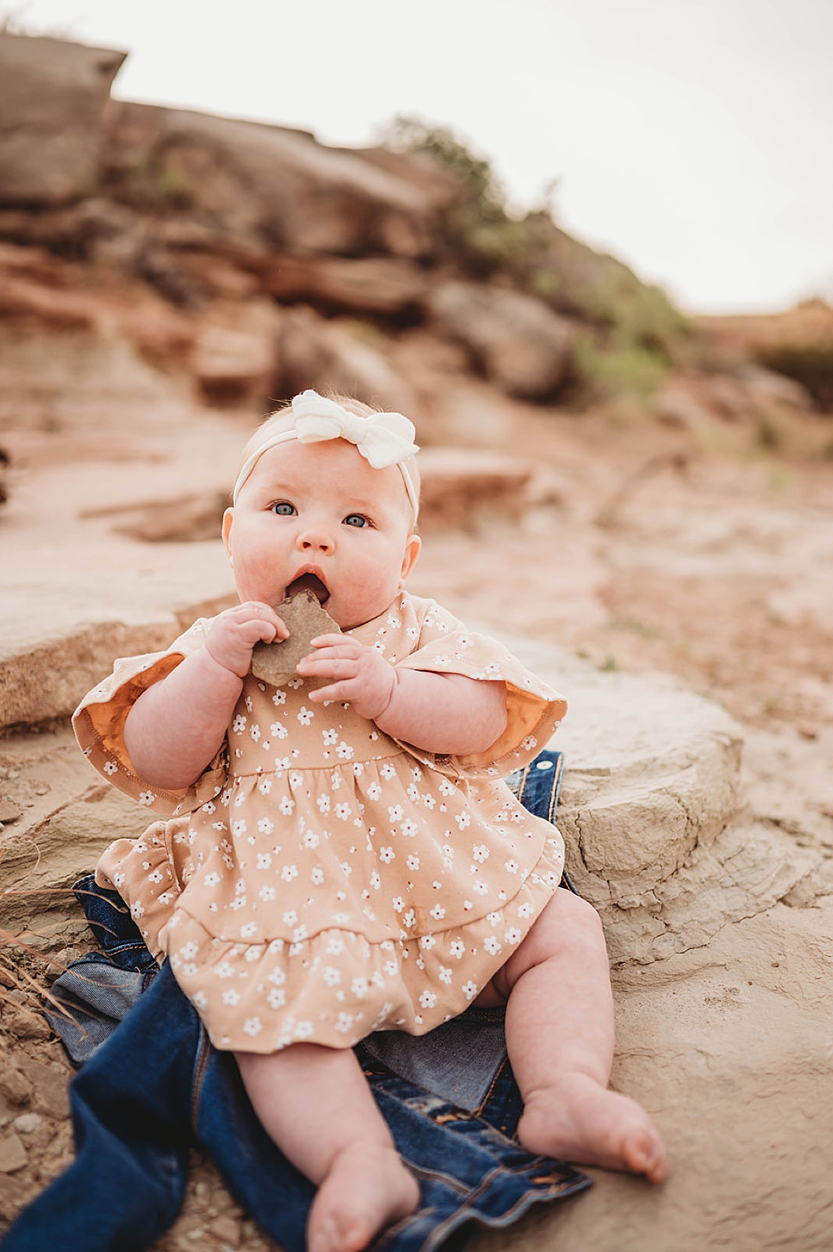 baby in flowered dress and headband with bow plays with rocks during family session with three feather photo co