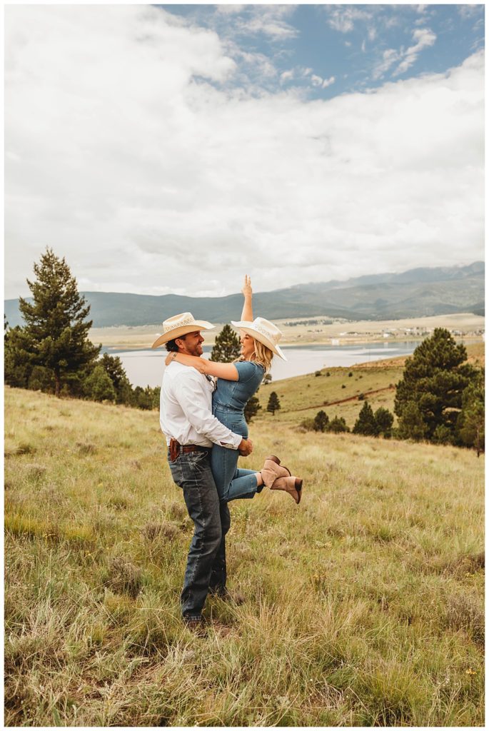 guy holds girl on grassy hill by Three Feather Photo
