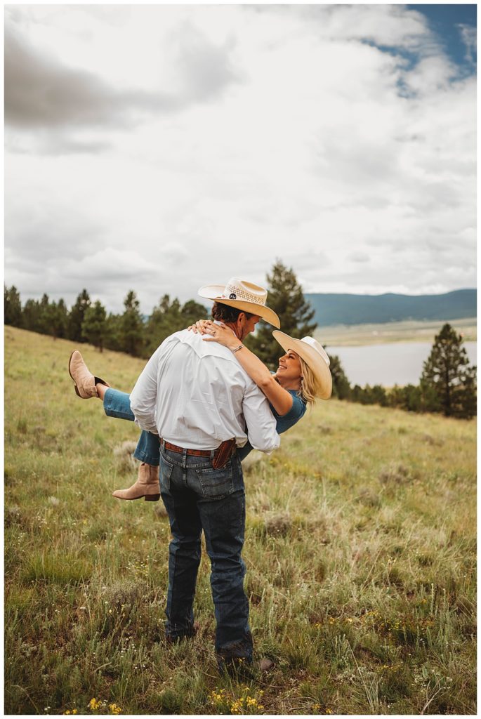man carries woman on grassy hill by Three Feather Photo