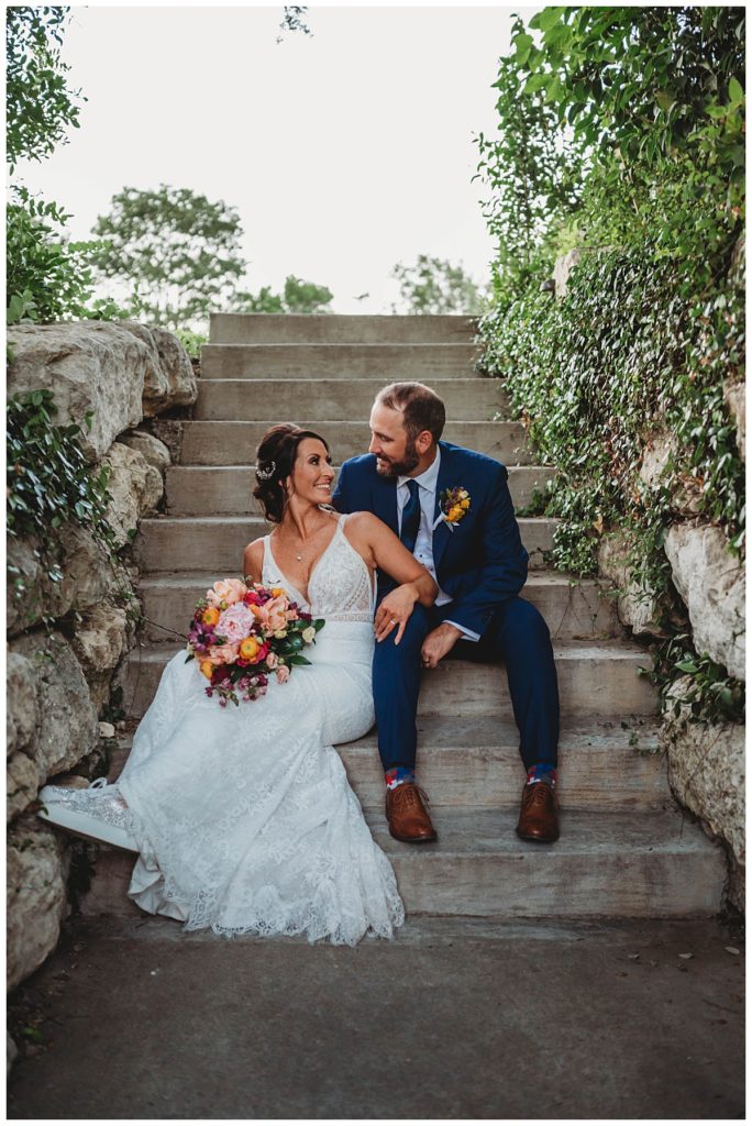 couple looks at each other sitting on stairs at Austin villa wedding