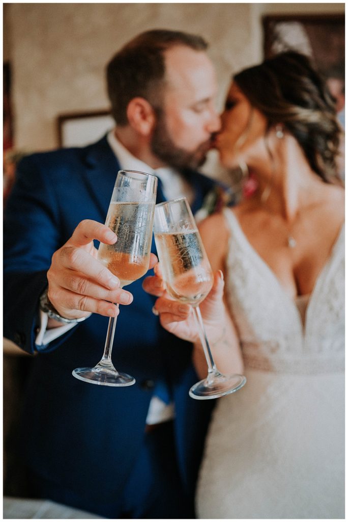 champagne glasses toasted as couple kisses at Austin villa wedding