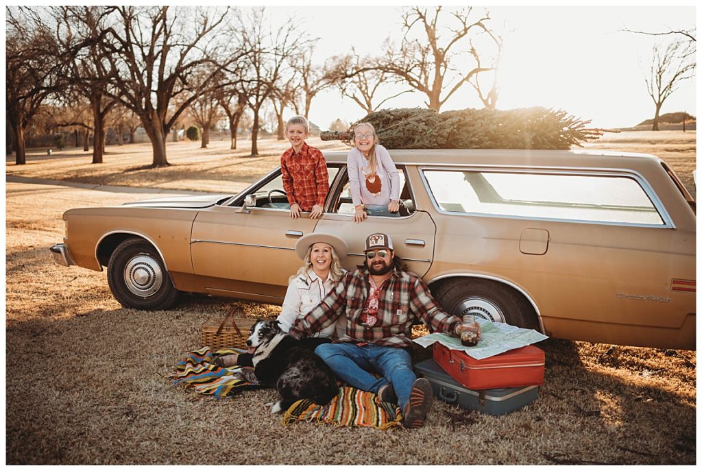 kids hang out of car while parents sit on blanket with dog at family session in Amarillo