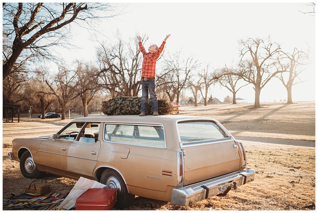 kid stands on roof of car looking at sky with hands up by Three Feather Photo