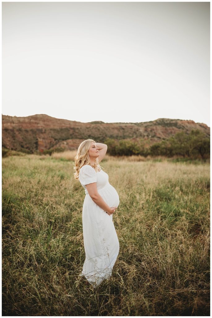 pregnant woman holds belly in meadow by Palo Duro family photographer