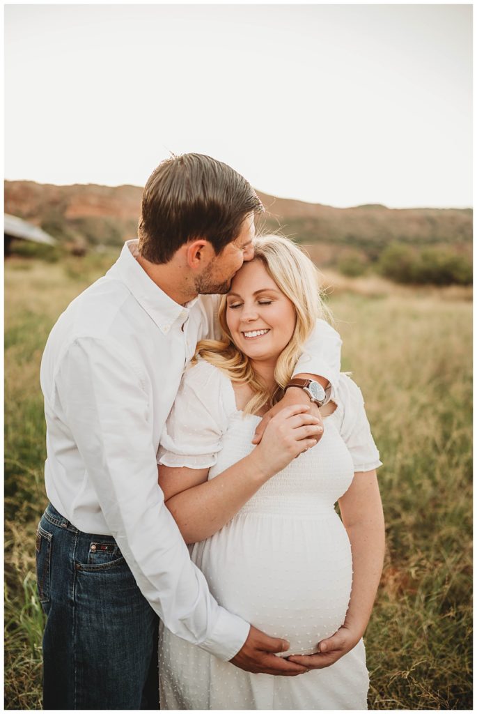 man puts arm around wife and kisses her at canyon maternity shoot