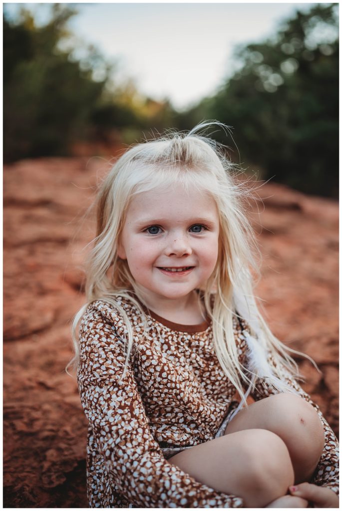 blond haired girl smiles sitting on rock by Three Feather Photo