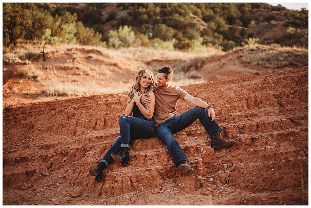 couple sits together on red rocks by Three Feather Co